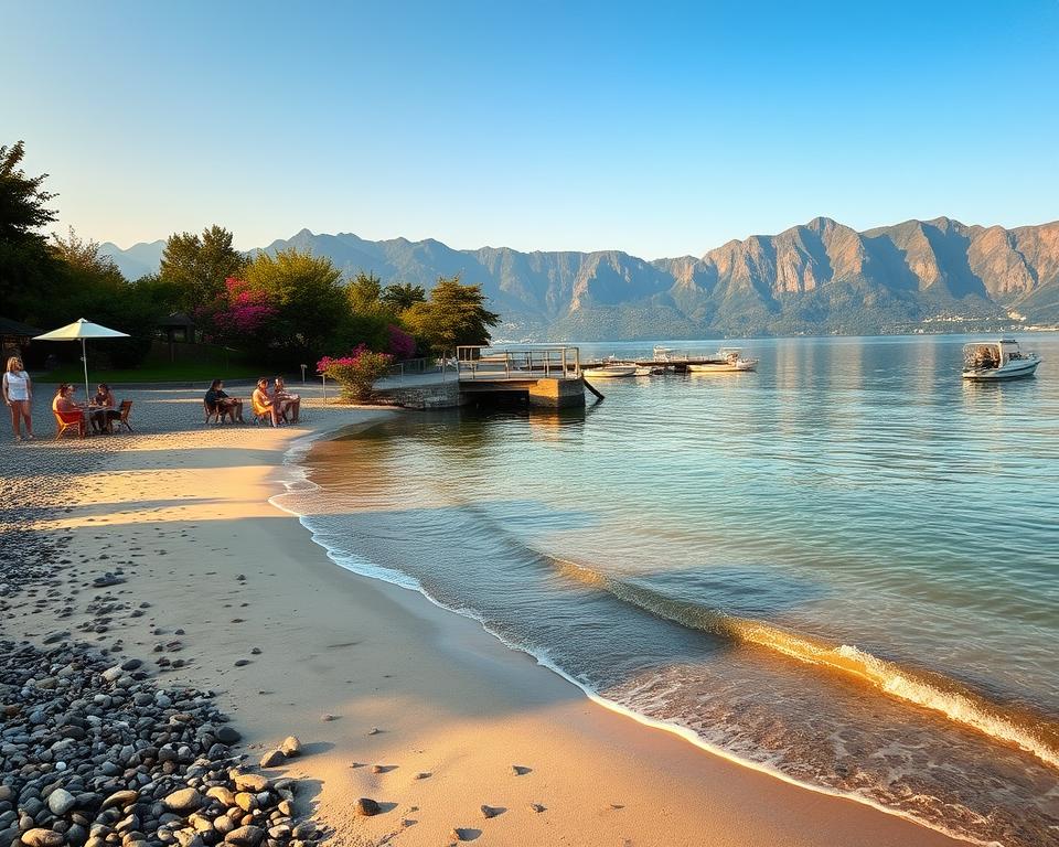A serene scene at Lake Garda showcasing a tranquil beach access point, with gentle waves lapping against the shore. In the foreground, a smooth sandy beach with scattered pebbles, illuminated by the warm glow of the late afternoon sun. A few families are enjoying picnics, with children playing nearby, all dressed in casual summer attire. In the middle ground, a wooden dock extends into the crystal-clear water, lined with small boats bobbing gently. Lush greenery borders the beach, with vibrant flowers adding pops of color. In the background, the majestic mountains rise, their silhouettes softened by the golden light of sunset, creating a peaceful and inviting atmosphere. The image captures the joy of a perfect day by the lake, emphasizing relaxation and nature's beauty.